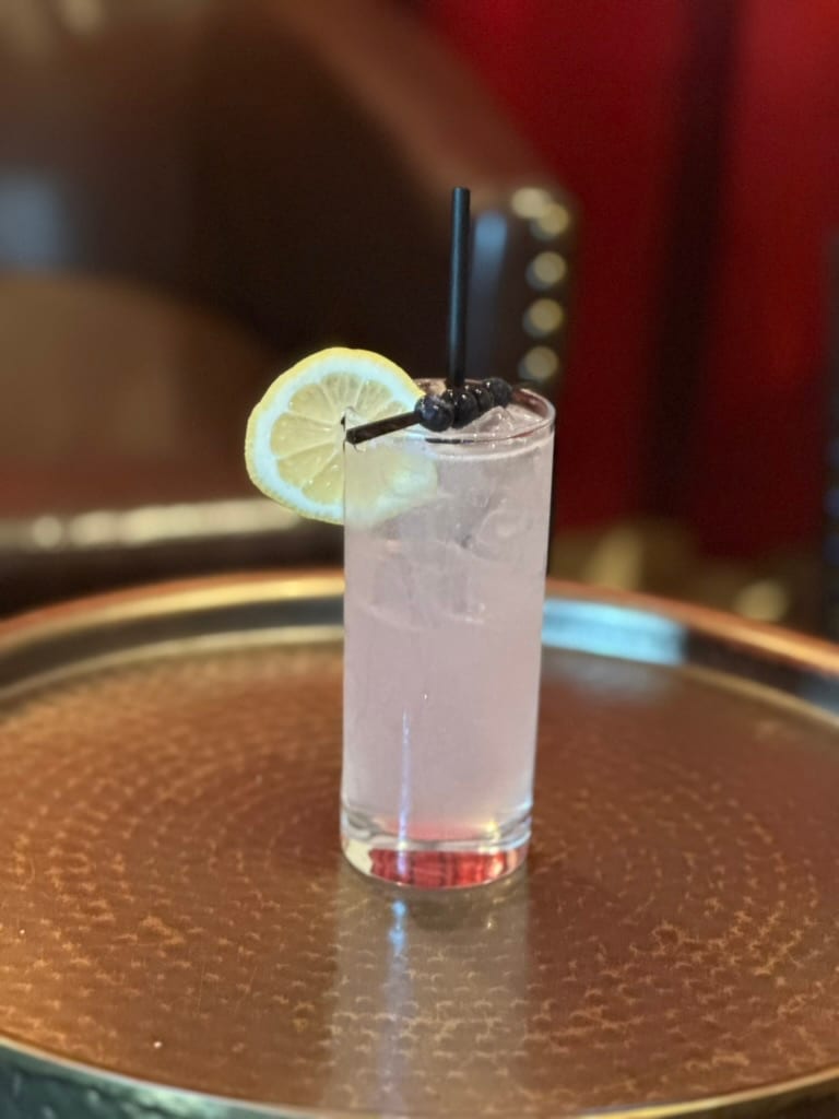 A highball with a lemon wheel on a hammered copper tray